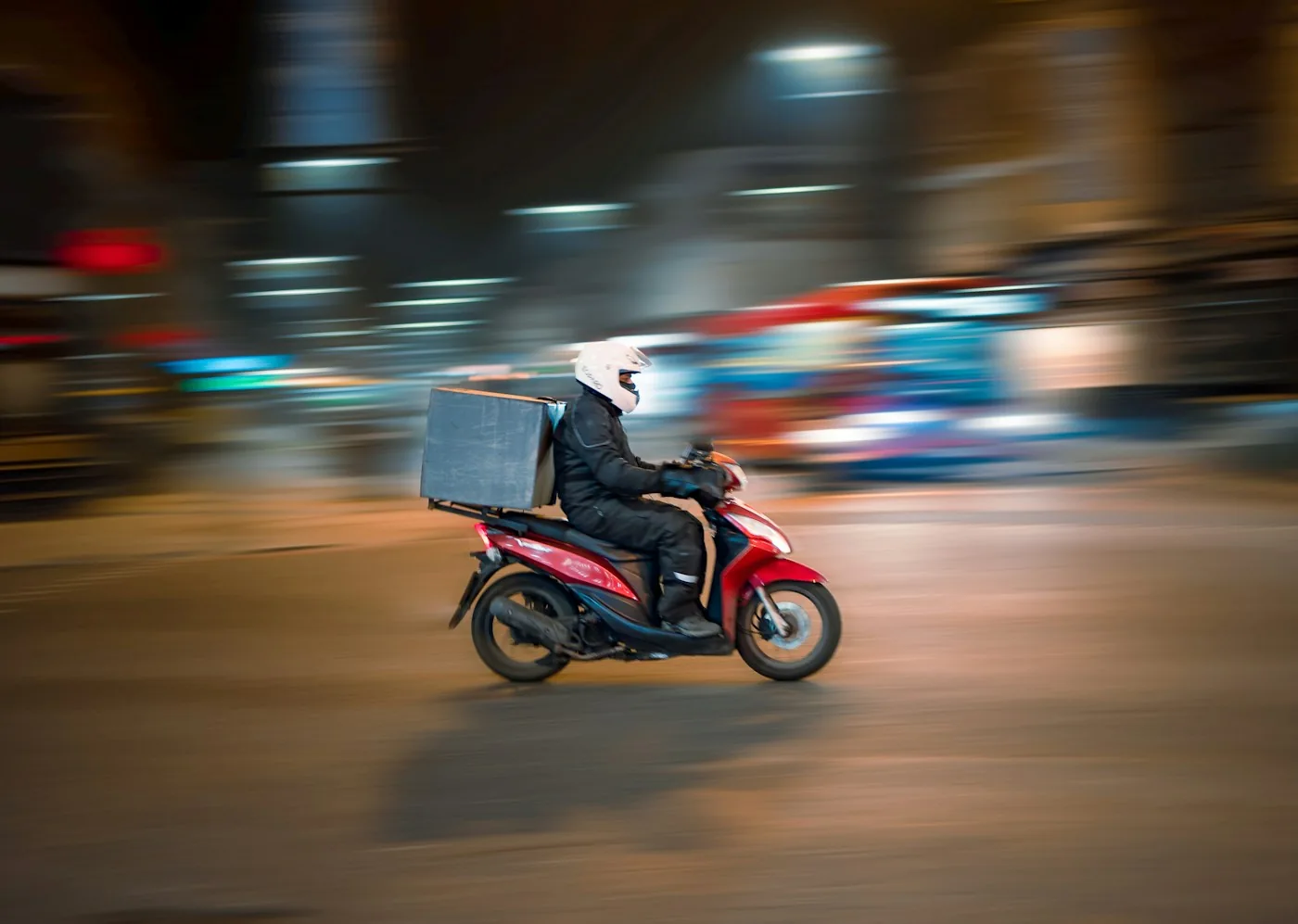 Repartidor en moto con caja de entrega circulando por la ciudad de noche